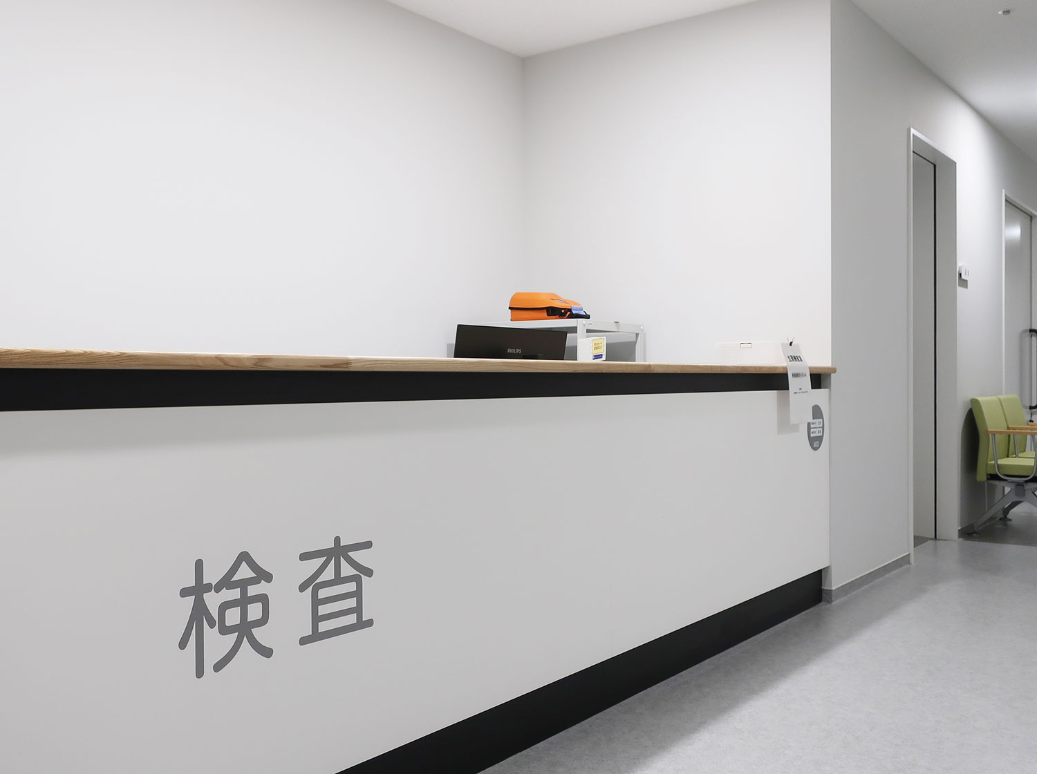 検査室の受付カウンター。白壁に「検査」の表示があり、医務室・検査設備の空間。